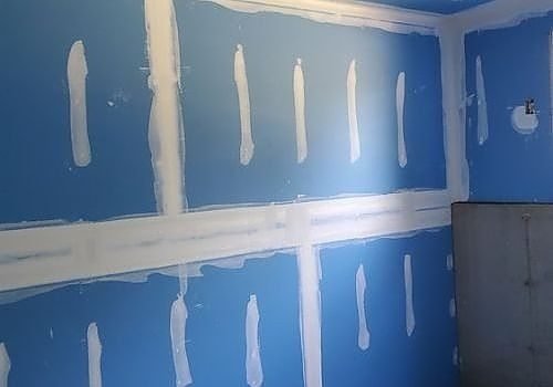 Blue drywall with white joint compound patches in a room under renovation.
