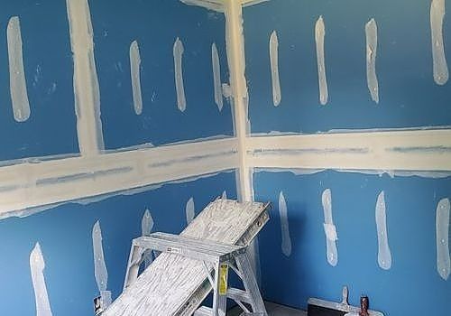 Partially painted blue room with white patch marks and a stepladder in the corner