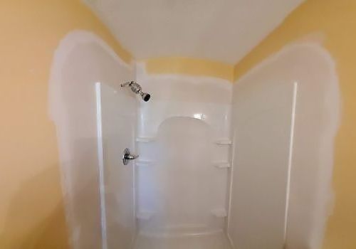 Partially painted shower stall with white primer and beige walls