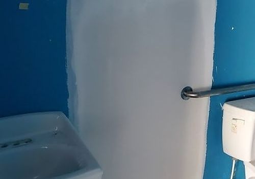 Small bathroom with blue walls, white shower curtain, sink, and towel bar next to a toilet tank.
