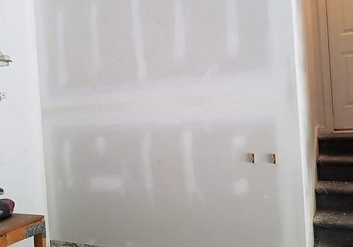 Unfinished drywall wall inside a room, with steps and a door on the right.