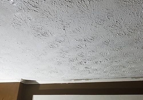 Textured white ceiling above a brown wall trim with a small corner seam visible