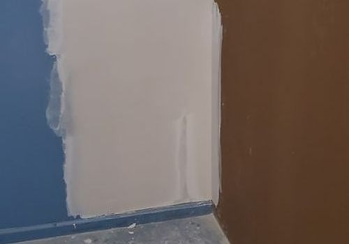 Partially painted interior corner with white, blue, and brown walls near a floor edge