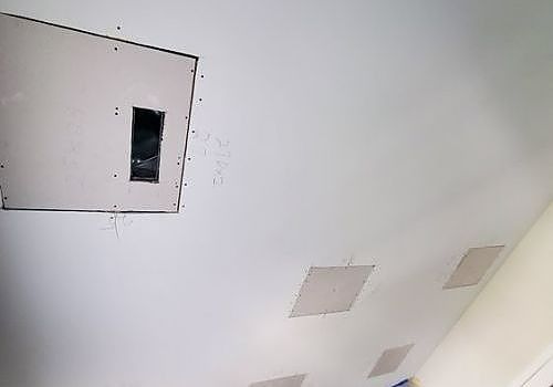 Ceiling with several square access panels, including one open panel with a dark opening.