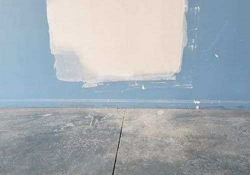 Blue wall with a large unfinished white patch above a gray concrete floor
