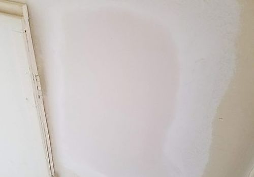 A white wall with a large, lighter patch of fresh paint or repair near the corner
