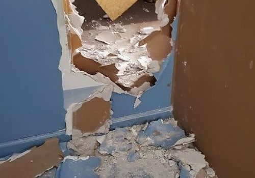 Damaged blue wall with a large hole and debris scattered on the floor