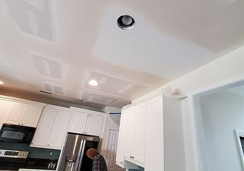 Kitchen with white cabinets and a person standing near a stainless steel refrigerator under a ceiling light.