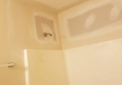 Partially tiled bathroom wall and shower area under construction, with beige drywall patches and a shower arm.