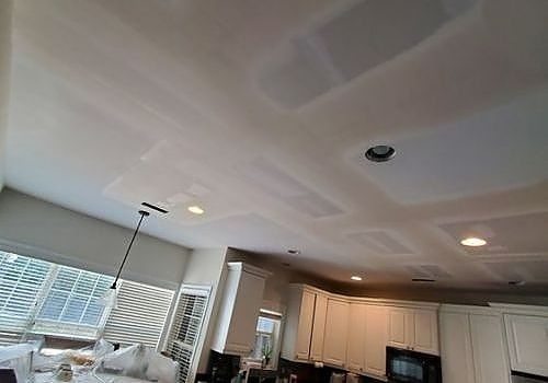 Ceiling with smoke detector and recessed lights above a bright kitchen and living room