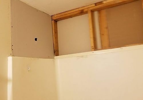 Partially built wall with exposed wooden framing and beige drywall above a white surface