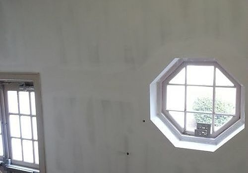 Plain white room with two windows, including an octagonal window showing greenery outside.