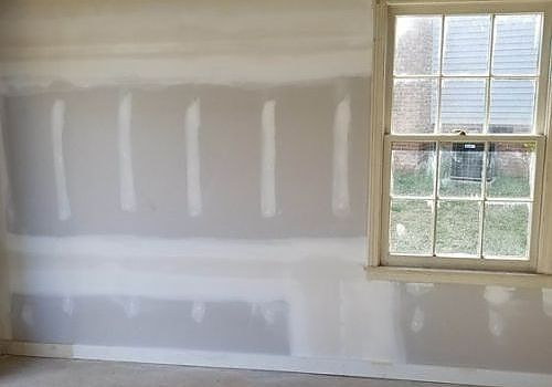Unfinished drywall with taped seams and a window in a room under renovation