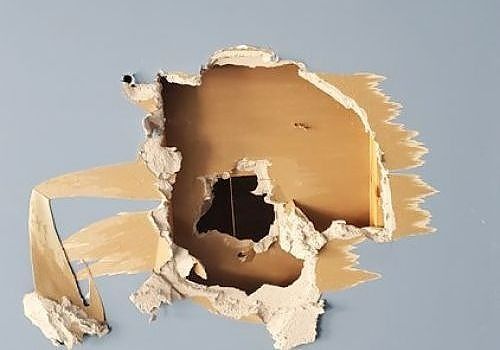 Torn cardboard opening in a tan panel, revealing a dark hole against a light gray background