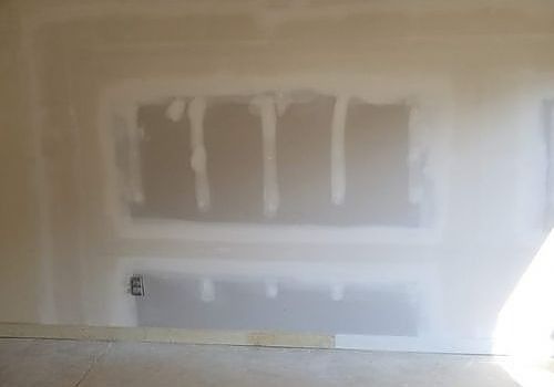 Primed drywall wall with taped patch areas and baseboard in a room under renovation