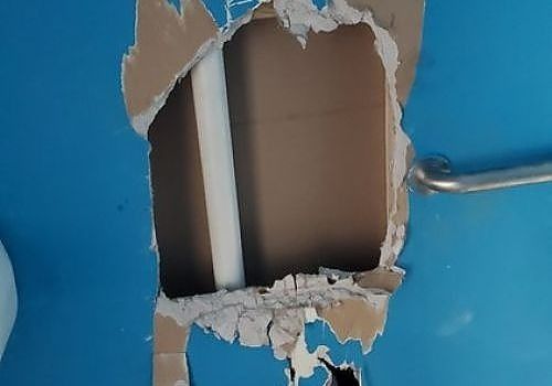 Wall with a large broken hole exposing beige interior and a metal conduit against blue paint