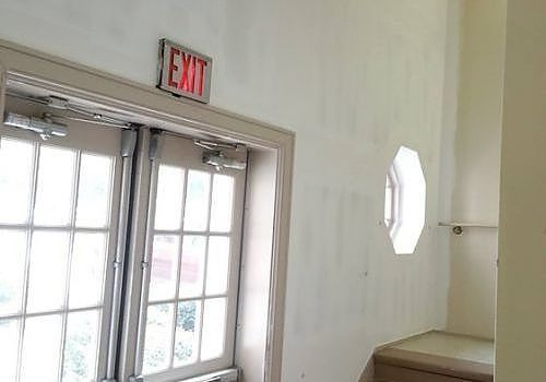 Interior wall with exit door and sign, and a small octagonal window on the right.