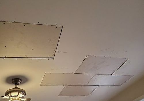 Ceiling with several missing or replaced tiles and a ceiling fan in the lower left corner