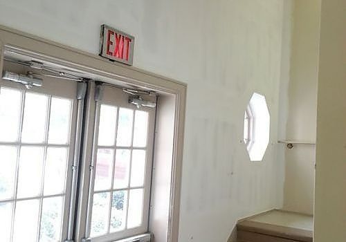Interior doorway with glass double doors, red EXIT sign, and octagonal window in a white hall