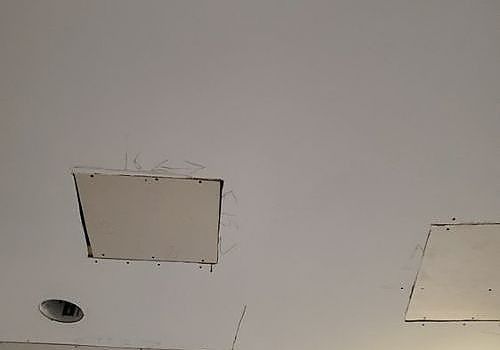 White ceiling with two unfinished square patches and a recessed light opening