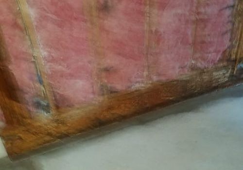 Pink and orange worn fabric panel leaning against a gray floor, with a rough wooden base