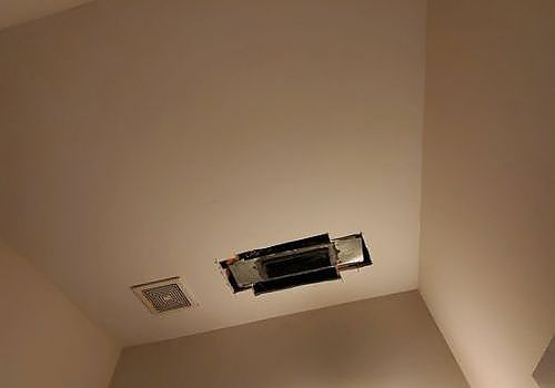 Ceiling corner with a damaged recessed light fixture and a nearby vent grille