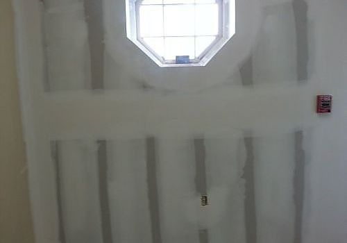 Unfinished interior wall with drywall seams and a small octagonal window letting in light