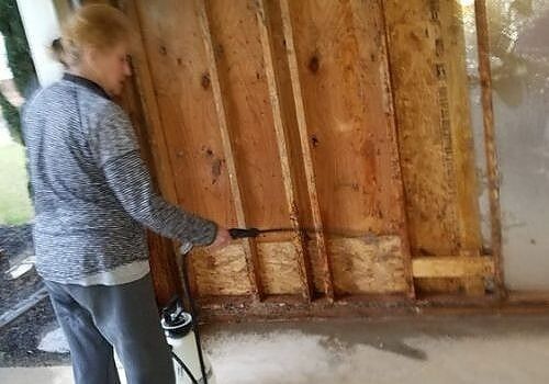 Person spraying a wooden wall with a paint sprayer in an unfinished room