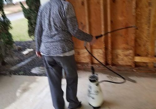 Person spraying a wooden wall with a backpack sprayer in a covered area