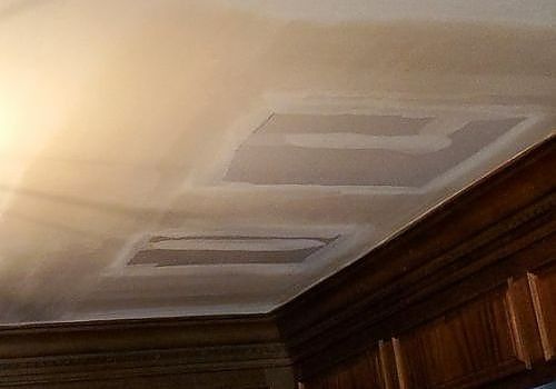 Ceiling with two rectangular vents and recessed panels above wood-paneled walls