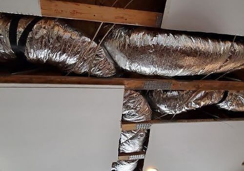 Metal HVAC ducts and foil insulation exposed in a ceiling opening