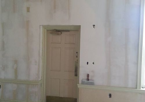 Empty room with pale walls, a closed door, and sunlight from a window on the right.