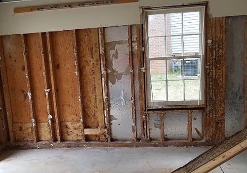 Partially stripped interior wall with exposed studs and a window in a room under renovation