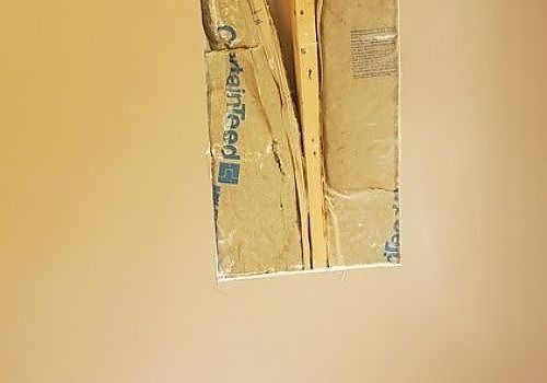 Small damaged section of beige wall with exposed insulation and taped plaster edges.