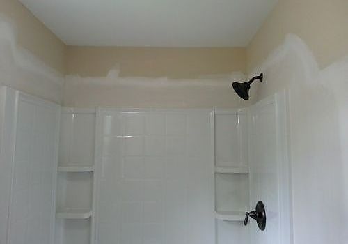 Empty white bathroom with a shower, built-in shelves, and black light fixtures on beige walls