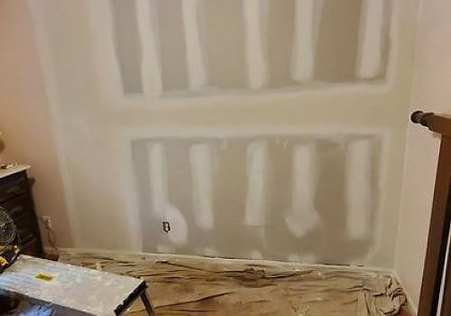 Unfinished drywall with white joint compound patches in a room under renovation, with drop cloths on the floor.