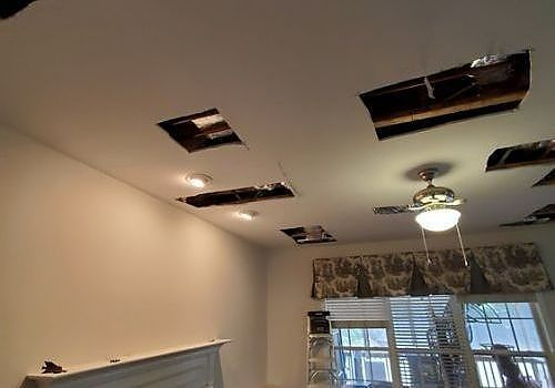 Ceiling with several missing light fixtures and exposed openings in a beige room near a window.