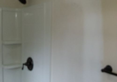 White shower stall with glass shelves and black grab bars on tiled walls