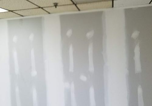 Rows of white drywall panels with taped seams in an unfinished interior room.