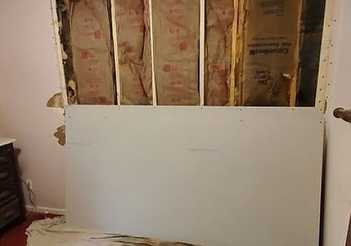 Partially renovated room with exposed insulation above a white wall panel
