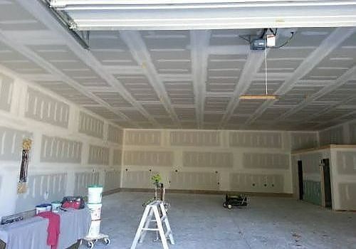 Large unfinished garage interior with drywall, concrete floor, ladder, and work items scattered around