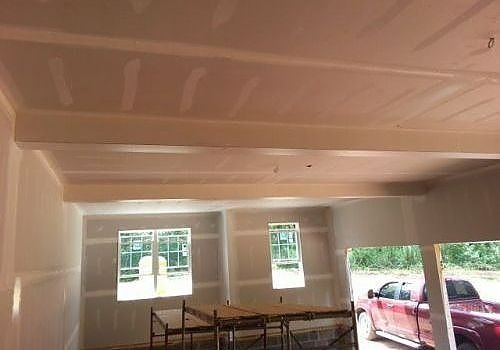 Unfinished interior with exposed ceiling, windows, tables, and a red car visible outside