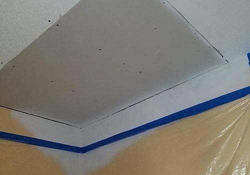 Painted ceiling patch taped off with blue painter’s tape and plastic sheeting below