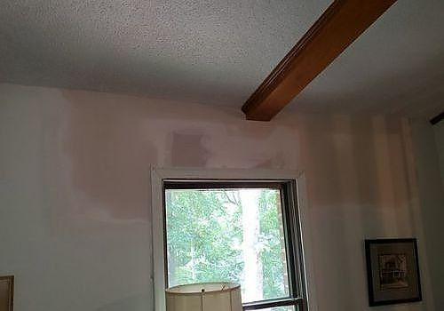 Interior wall with a window, wooden ceiling beam, and framed art hanging on the right.