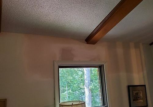 Interior room with vaulted ceiling, exposed beam, and a window showing trees outside.