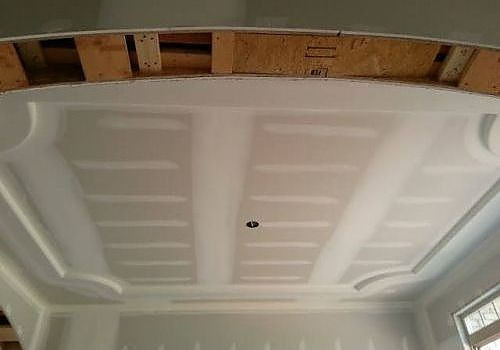 Interior view of a white molded ceiling panel with a small black hole, framed by exposed wooden beams