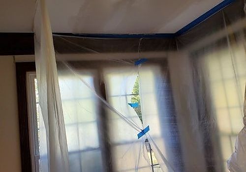 Room under renovation with plastic sheeting over windows and a ladder in the center
