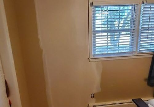 Bare beige wall with a window and blinds, plus a radiator below.