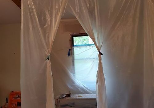 Plastic sheeting draped over a doorway, with a small window visible beyond it in a room under renovation