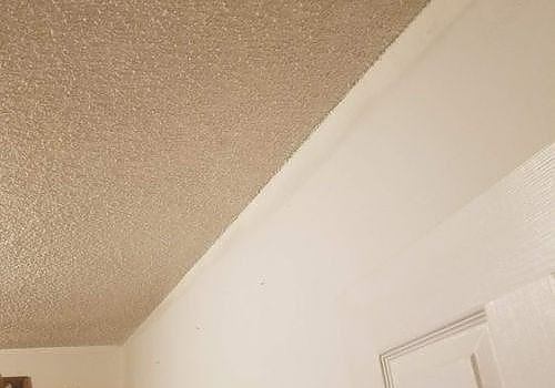 Textured beige ceiling meeting white wall above a door frame